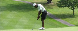 photo of a black man in shorts and white cap playing golf