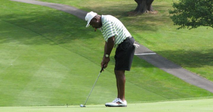 photo of a black man in shorts and white cap playing golf
