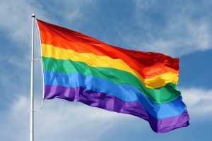 Large rainbow flag proudly waving against the blue sunny skies