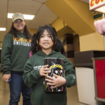 little girl in Mason gear holding popcorn. Big sister or mom in the back, also in Mason gear.