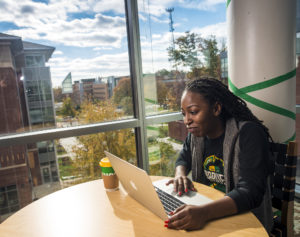 Young black woman sits using a computer next to a window overlooking Mason's Campus