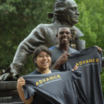 Students with ADVANCE t-shirts smiling in front of the George Mason statue