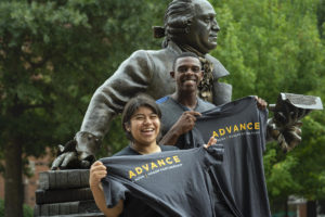 Students with ADVANCE t-shirts smiling in front of the George Mason statue