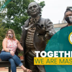 Two masked students around the George Mason statue