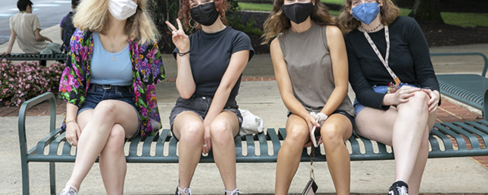 4 masked women on a bench on campus