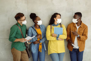 Multi-ethnic group of college students with face masks communicating against the wall.