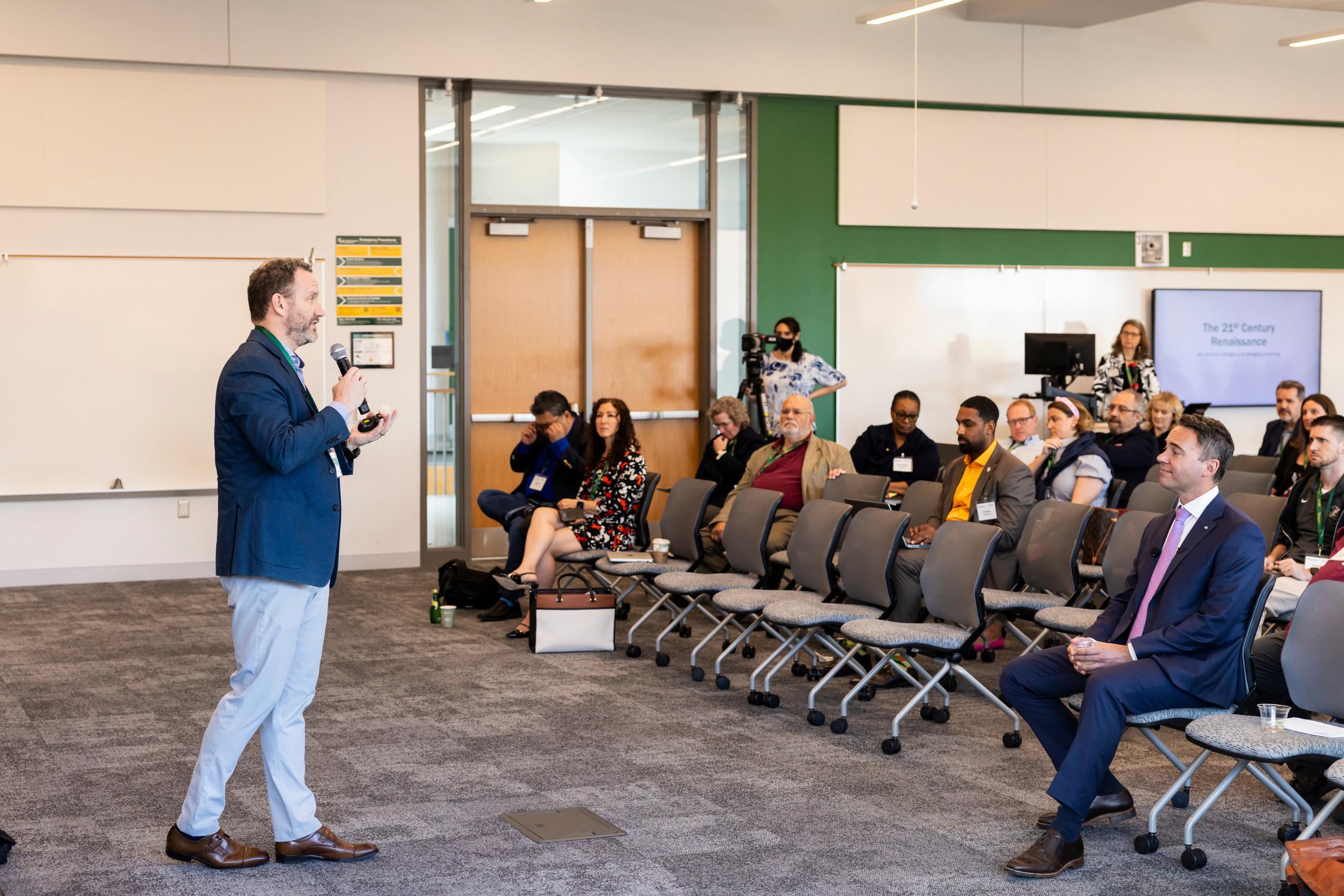 George Mason faculty, staff, and students in a class room sitting in roller chairs listening to a presenter.