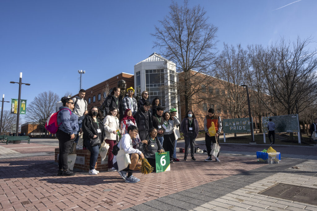 Students gather in front of Johnson Center. Holding a sign that says "6"