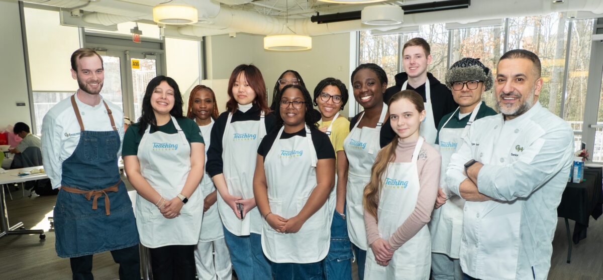 Students wearing Teaching Kitchen aprons stand with campus chefs for a group photo during a Mason Dining Teaching Kitchen event.