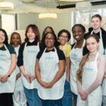 Students wearing Teaching Kitchen aprons stand with campus chefs for a group photo during a Mason Dining Teaching Kitchen event.