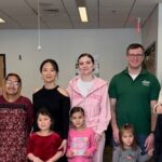 A group of student parents, staff members, and children pose together for a photo at a CSS Student Parent and Caregiver Meetup. A "Kids Zone" sign is visible in the background.