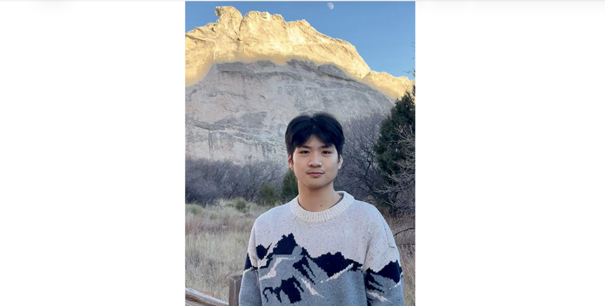 Jonathan Fang stands outdoors in front of a large sandstone rock formation at golden hour, wearing a cream sweater with a mountain pattern. A crescent moon is visible in the sky above the cliff.