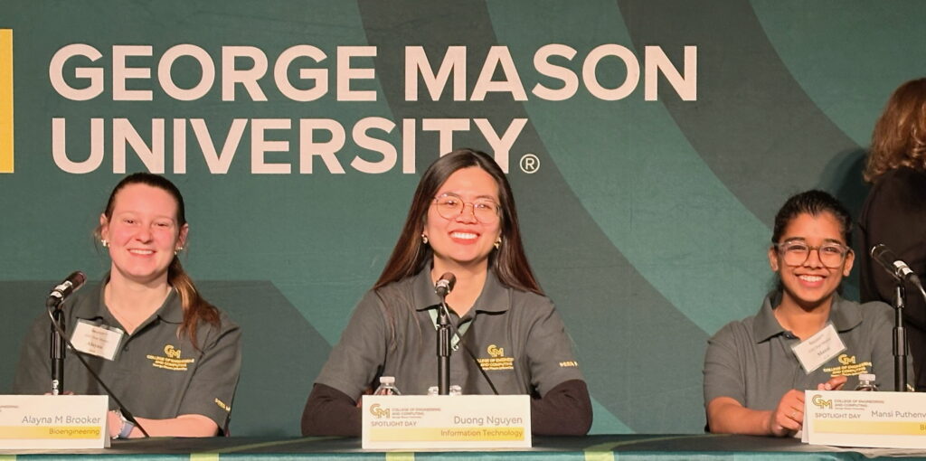 From left, Alayna M. Brooker, Duong Thuy Nguyen, and Mansi Puthenveettil sit at a panel table wearing gray College of Engineering and Computing polos, each with a name placard in front of them. A large George Mason University backdrop is visible behind them. The event signage reads "Spotlight Day."