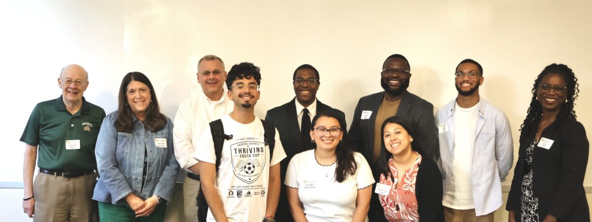Ten people stand in two informal rows in front of a whiteboard, smiling at the camera. From left to right: Thomas Snee, Rachel Sweeney, Thomas Ammazzalorso, Andres Curtin Campos, Philip Wilkerson, Jenniffer Andino Cruz, Stephanie Ayala, Jeremy Rogers, Cedric Price, and Alicia Brown.